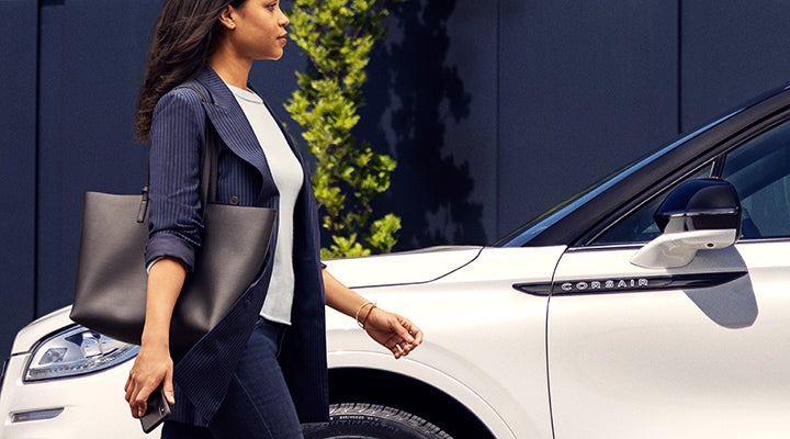 A woman approaches a 2024 Lincoln Corsair® SUV while holding a smartphone. | Varsity Lincoln in Novi MI
