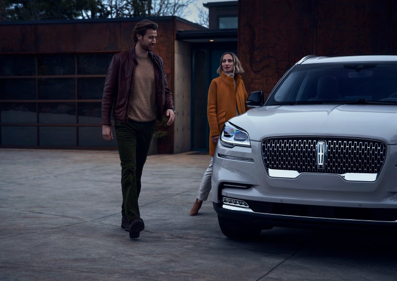 A man and a woman approaching a 2024 Lincoln Aviator® SUV, which illuminates certain lights when they are close | Varsity Lincoln in Novi MI