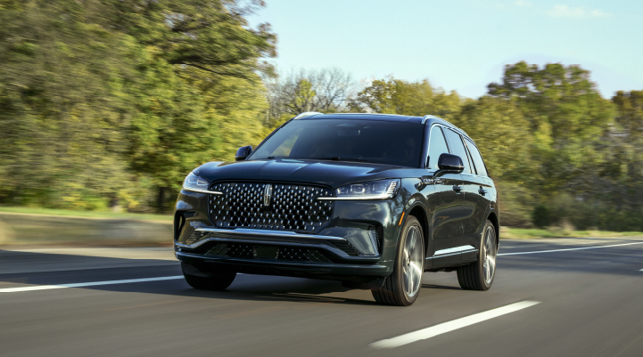 A 2025 Lincoln Black Label Aviator® SUV is being driven down a road lined with trees. | Varsity Lincoln in Novi MI