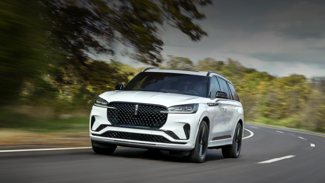 A white 2025 Lincoln Aviator® SUV is being driven down a road lined with trees. | Varsity Lincoln in Novi MI