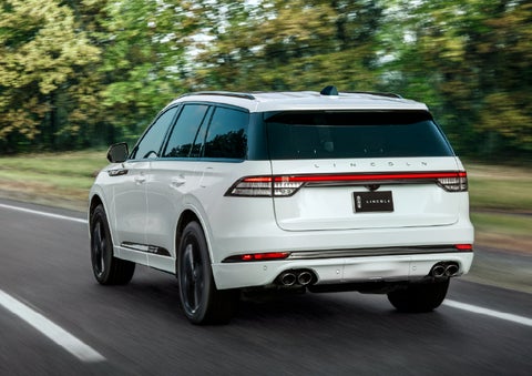A white 2026 Lincoln Aviator® SUV is being driven away down a road lined with colorful trees. | Varsity Lincoln in Novi MI