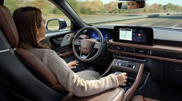 A 2026 Lincoln Aviator® SUV is being driven hands-free on a highway near a forest | Varsity Lincoln in Novi MI