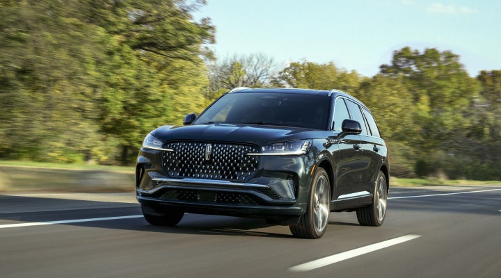A 2026 Lincoln Black Label™ Aviator® SUV is being driven down a road lined with trees. | Varsity Lincoln in Novi MI