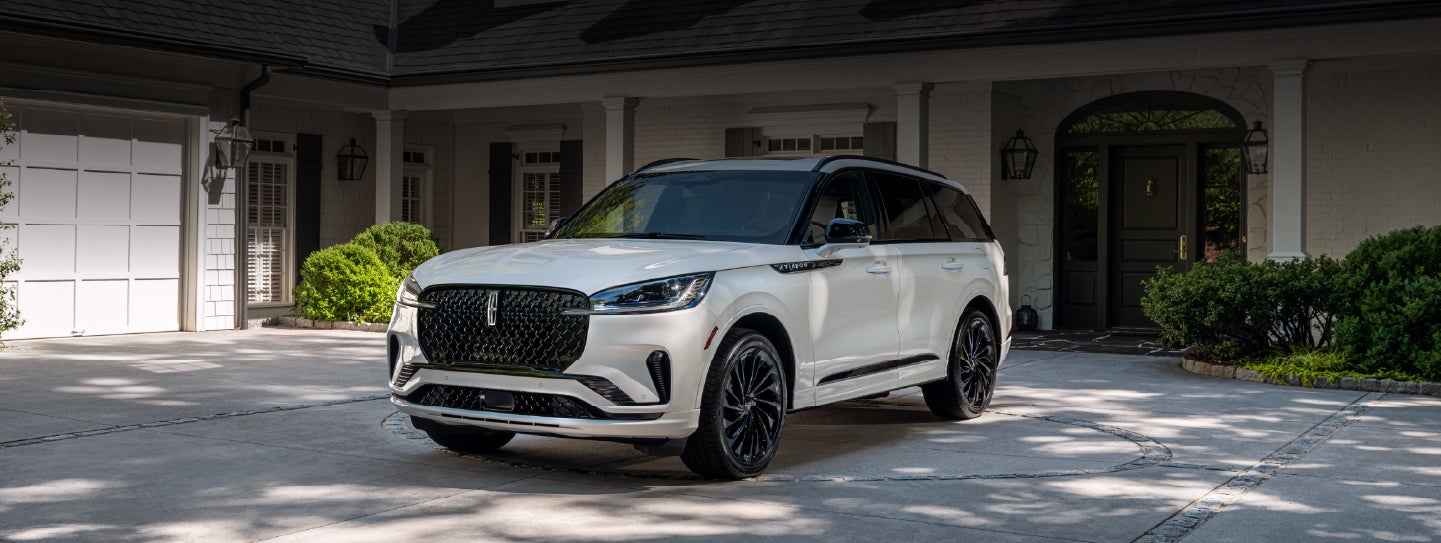 A white 2026 Lincoln Aviator® SUV is parked in the driveway of a luxury home. | Varsity Lincoln in Novi MI