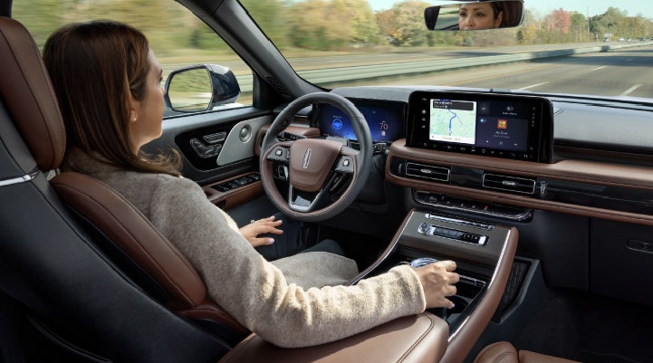 A 2027 Lincoln Aviator® SUV is being driven hands-free on a highway lined with trees. | Varsity Lincoln in Novi MI