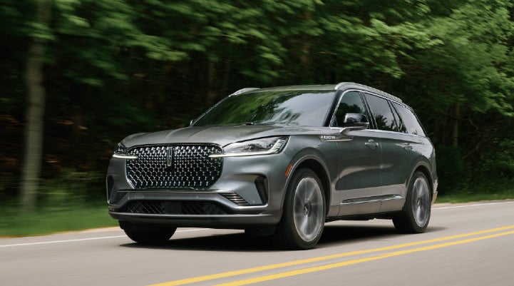 A 2027 Lincoln Aviator® SUV is being driven down a road lined with trees. | Varsity Lincoln in Novi MI